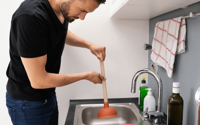 Man trying to unblock a blocked drain with a plunger